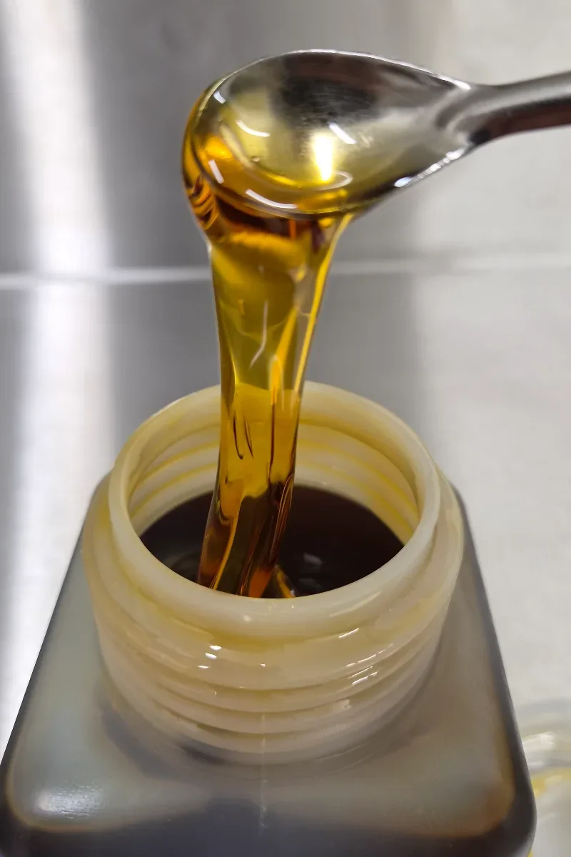 Golden, viscous Broad Spectrum distillate poured from a spoon into a jar on a stainless steel worktop