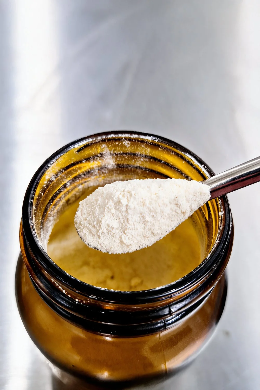 Poudre crème de CBDA dans un pot en verre ambré, prélevée à la cuillère inox
