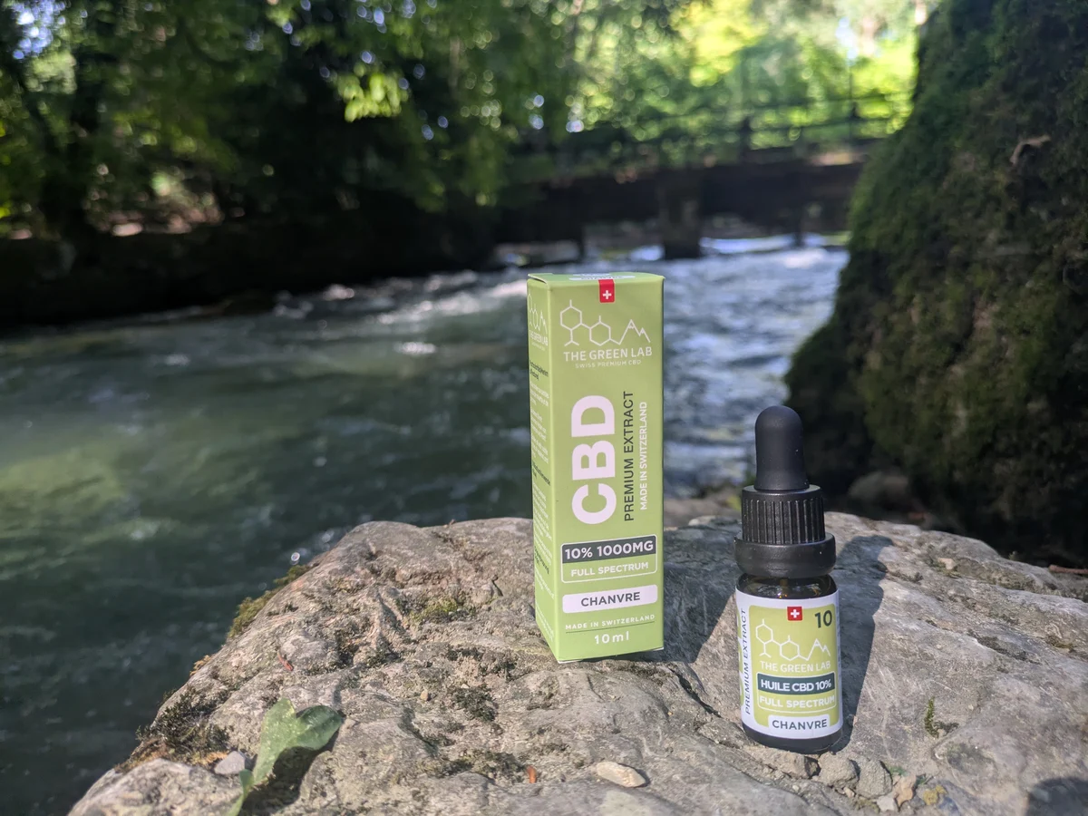 Dropper bottle of 10% CBD Hemp oil and its light green box on a rock at the edge of a river