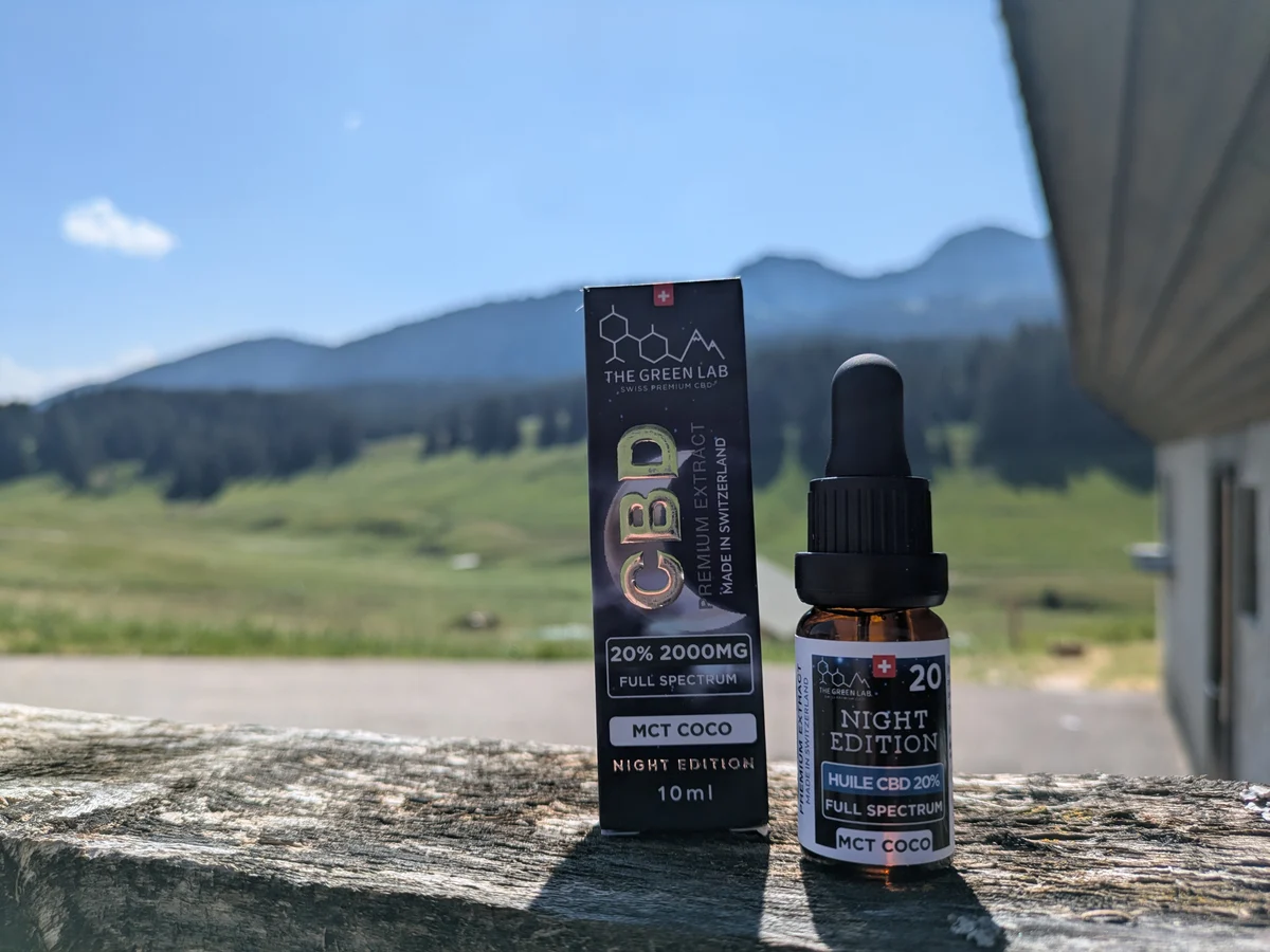 Schachtel und Flasche CBD-Öl Night Edition 20 % auf einer Mauer, Weiden und Wälder im Hintergrund