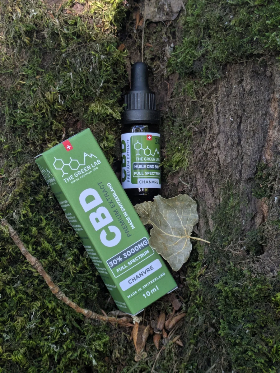 Box and bottle of Chanvre 30% CBD oil on moss at the foot of a tree