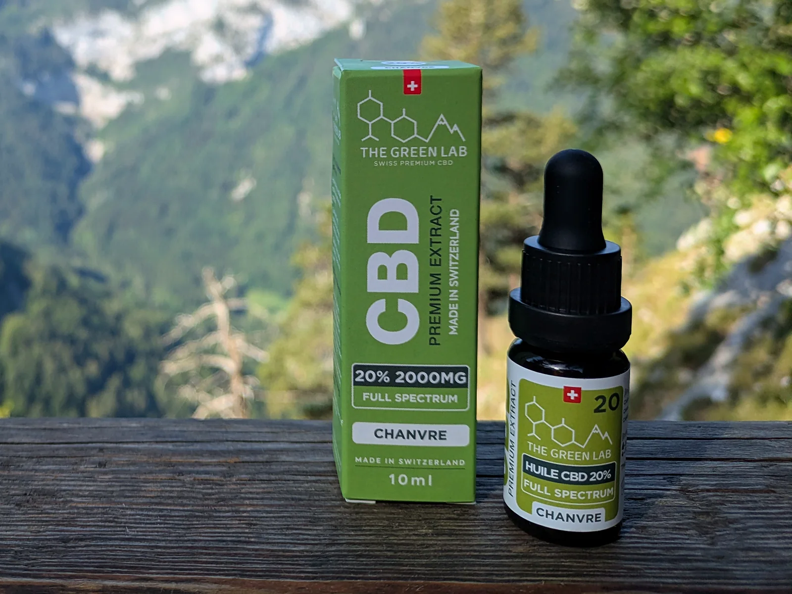 Huile CBD Chanvre 20 % et son étui posés sur un muret, montagnes en arrière-plan