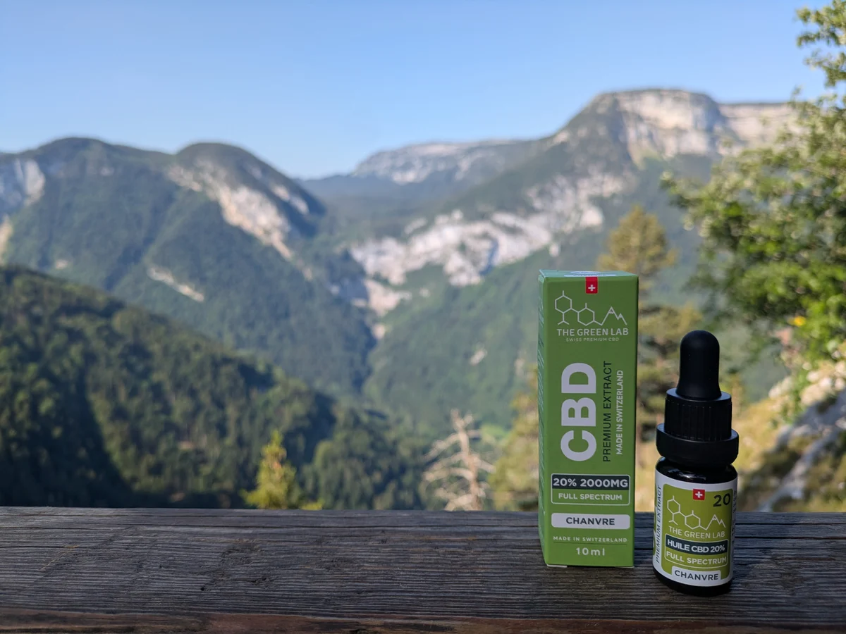 Huile CBD Chanvre 20 % et son étui posés sur un muret, montagnes en arrière-plan