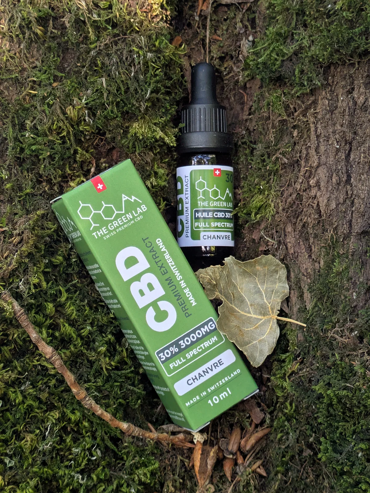 Étui et fiole d'huile CBD Chanvre 30 % posés sur la mousse au pied d'un arbre