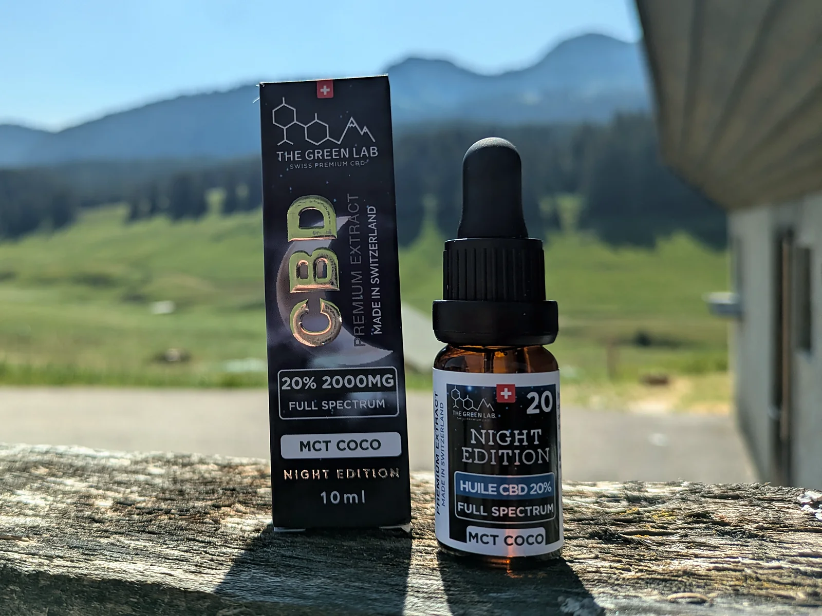 Étui et fiole d'huile CBD Night Edition 20 % sur un muret, pâturages et forêts en arrière-plan