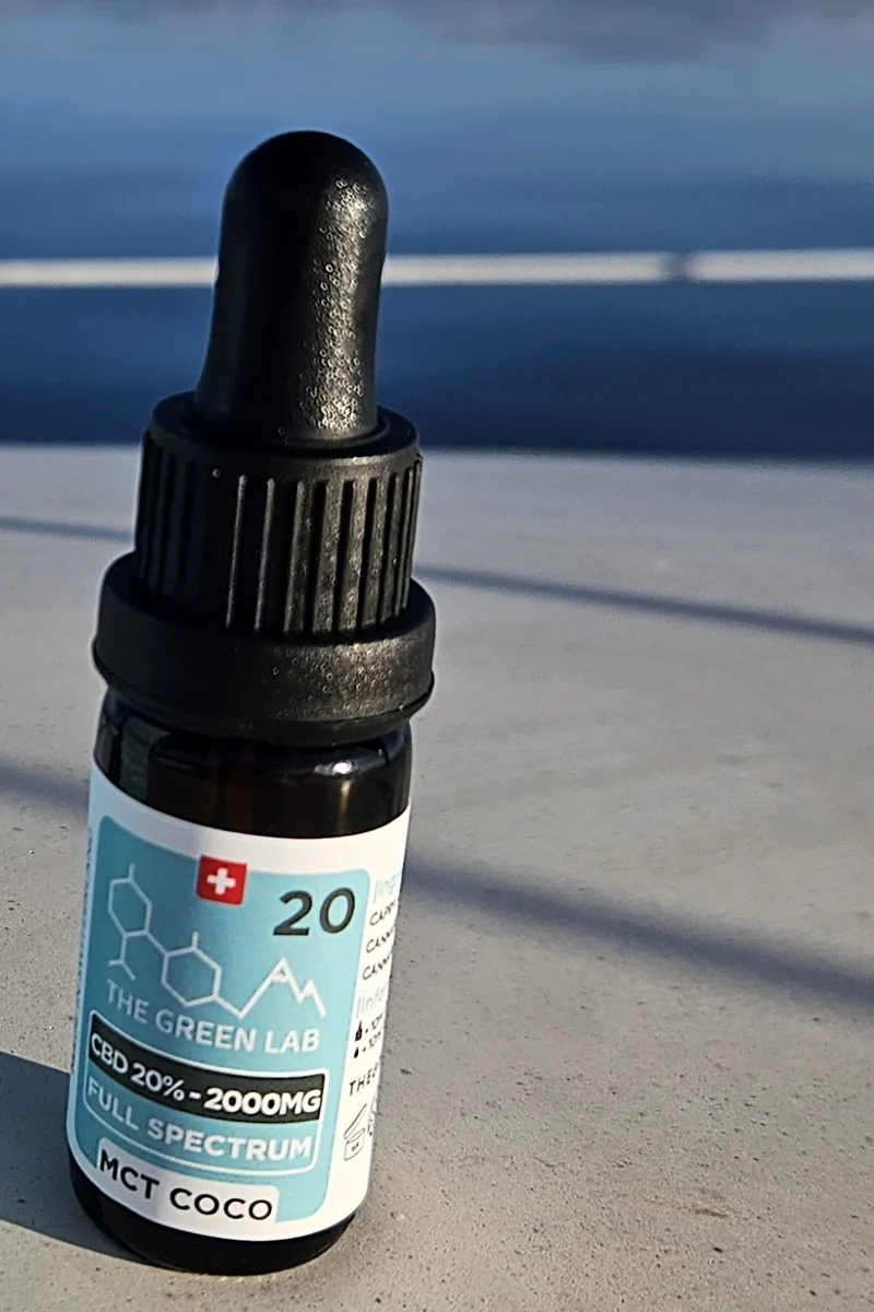 Flacon compte-gouttes d'huile CBD Sublime 20 % sur MCT de coco, posé sur un muret au bord du lac