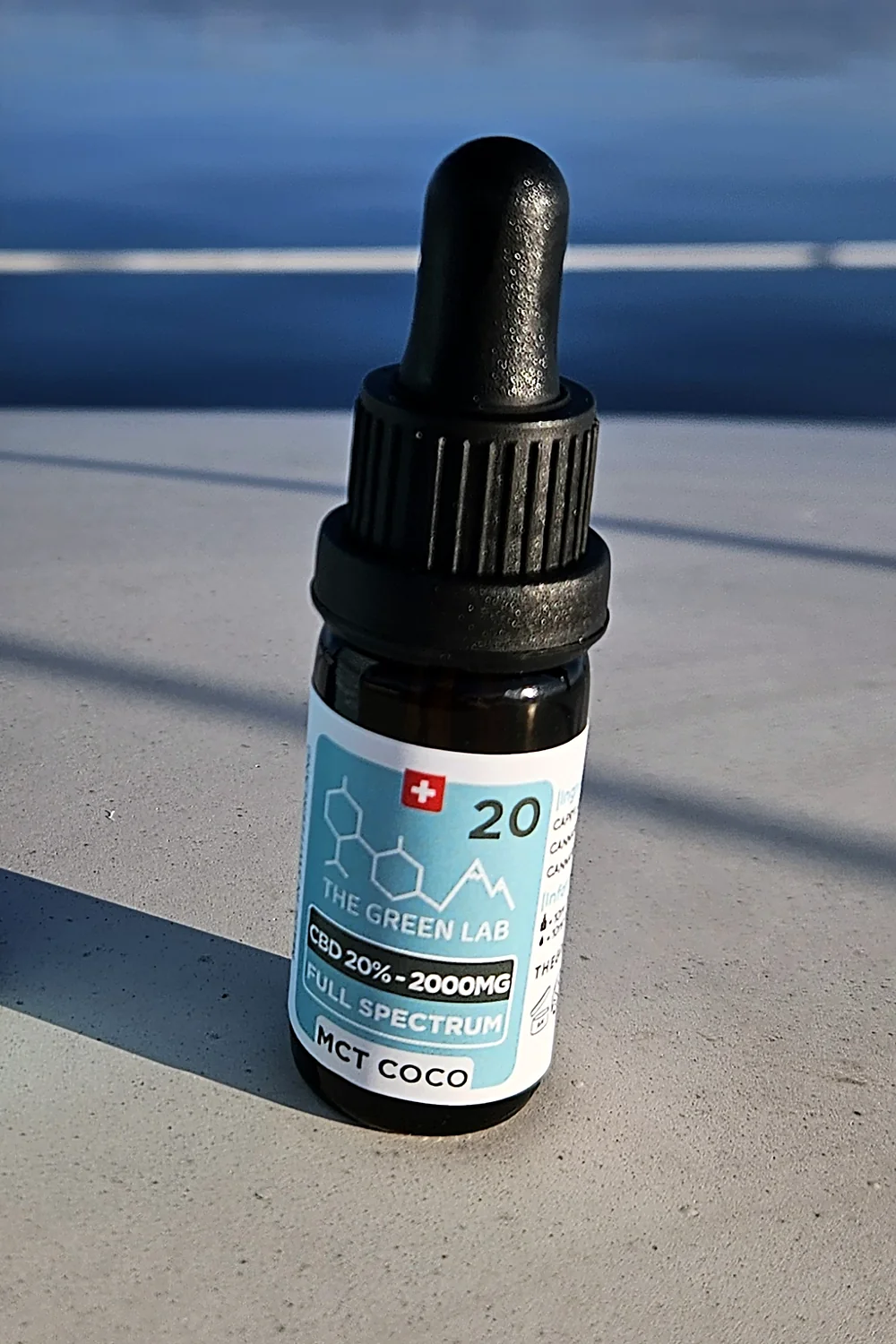 Flacon compte-gouttes d'huile CBD Sublime 20 % sur MCT de coco, posé sur un muret au bord du lac