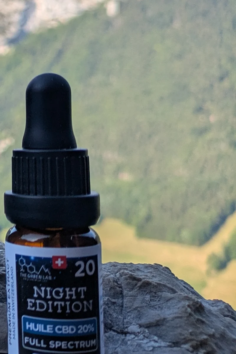 Flacon compte-gouttes en verre ambré d'huile CBD Night Edition 20 %, posé sur un rocher face aux montagnes