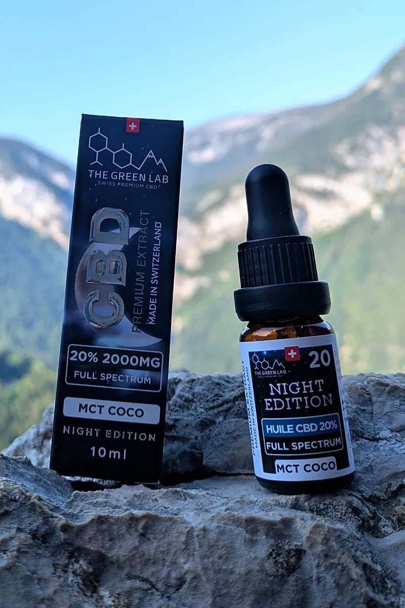 Flacon compte-gouttes en verre ambré d'huile CBD Night Edition 20 % et son étui, posés sur un rocher face aux montagnes