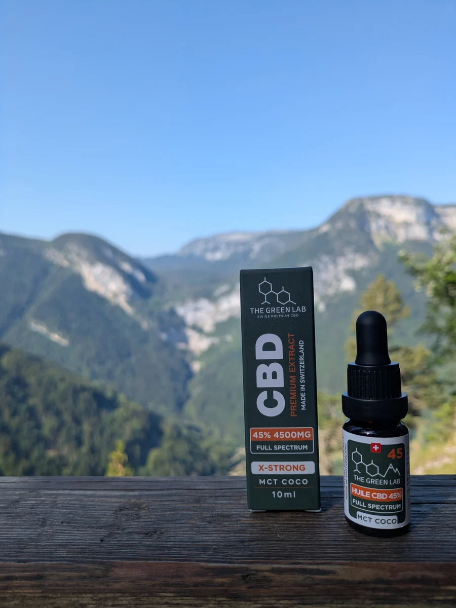 Flacon compte-gouttes d'huile CBD X-Strong 45 % Full Spectrum et son étui anthracite et orange, devant un paysage de montagne