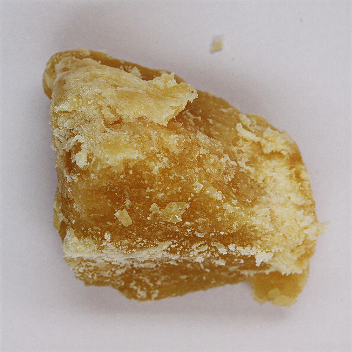 Piece of crystallised yellow CBD distillate at 89% on a light background